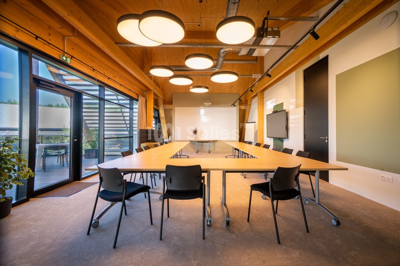 Salle de réunion lumineuse avec une grande table en bois en forme de U, des chaises noires et des luminaires modernes.