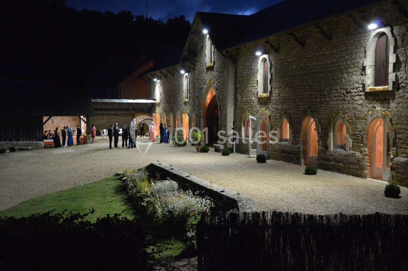 Cour éclairée d'un bâtiment en pierre avec des fenêtres illuminées, des invités rassemblés en soirée.