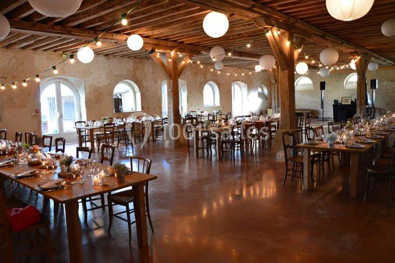 Salle de réception rustique avec tables en bois dressées, guirlandes lumineuses et lanternes suspendues.
