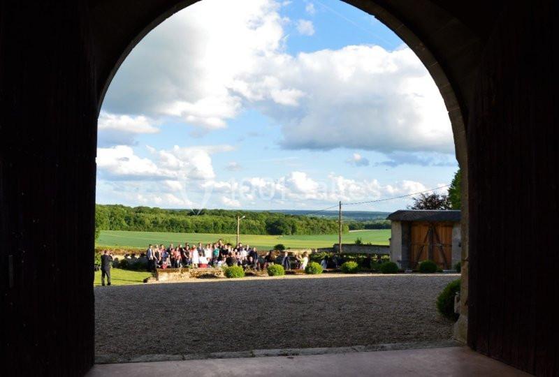 Vue sur un rassemblement en extérieur dans un paysage rural, encadrée par une arche en pierre.