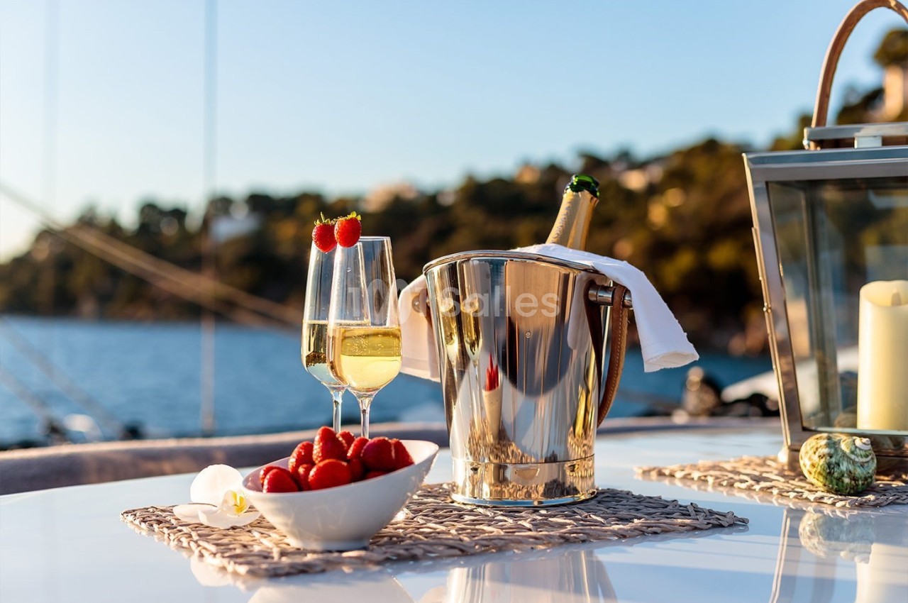 Seau à champagne, flûte remplie, fraises et bougie sur une table avec vue sur un paysage côtier ensoleillé.