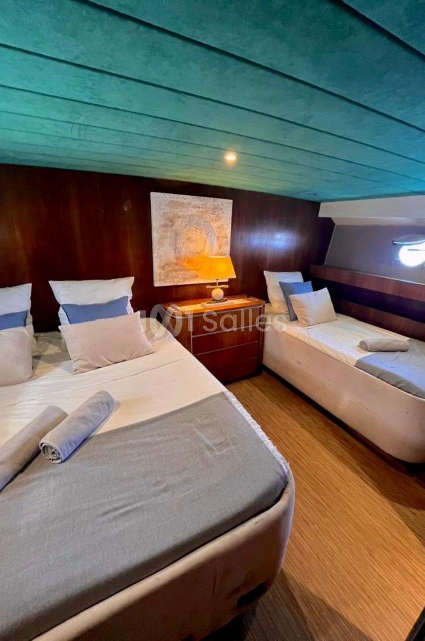 Cabine avec un lit double, un lit simple, des draps pliés, une lampe allumée et un plafond bleu.