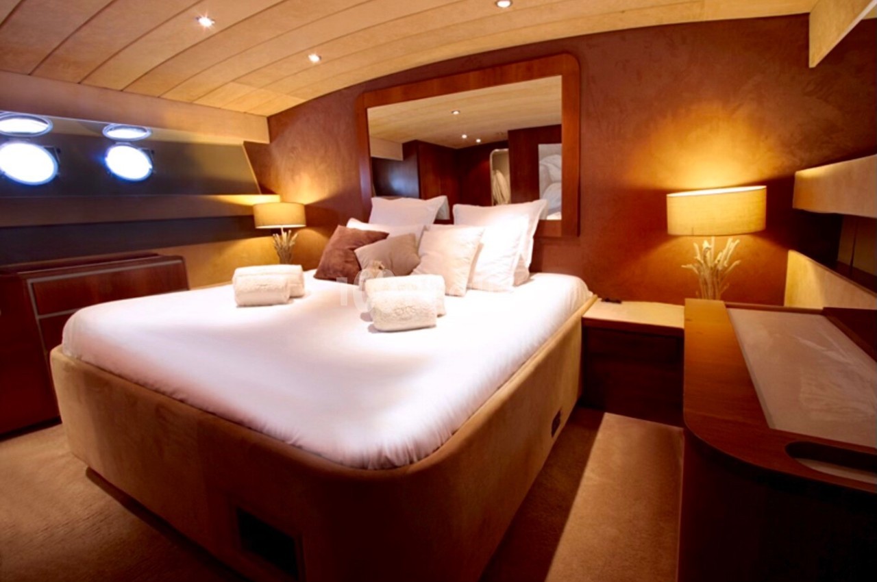 Cabine de bateau avec lit double, draps blancs, coussins décoratifs, éclairage chaleureux et hublots ronds.