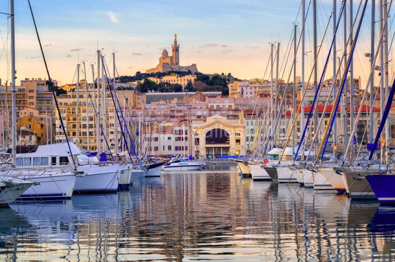 Vue sur le Vieux-Port de Marseille avec des voiliers amarrés et la basilique Notre-Dame de la Garde en arrière-plan.