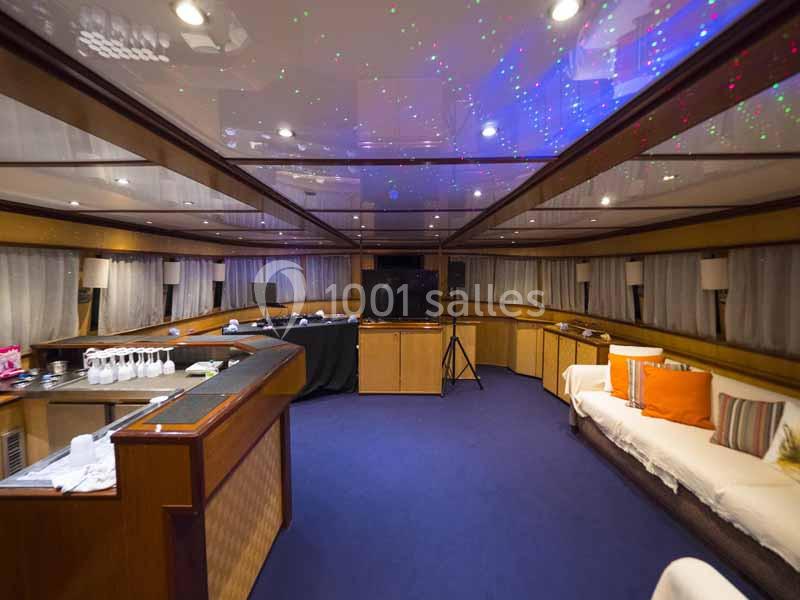 Intérieur d'un yacht avec un salon spacieux, canapé, bar, éclairage tamisé et plafond décoré de lumières colorées.