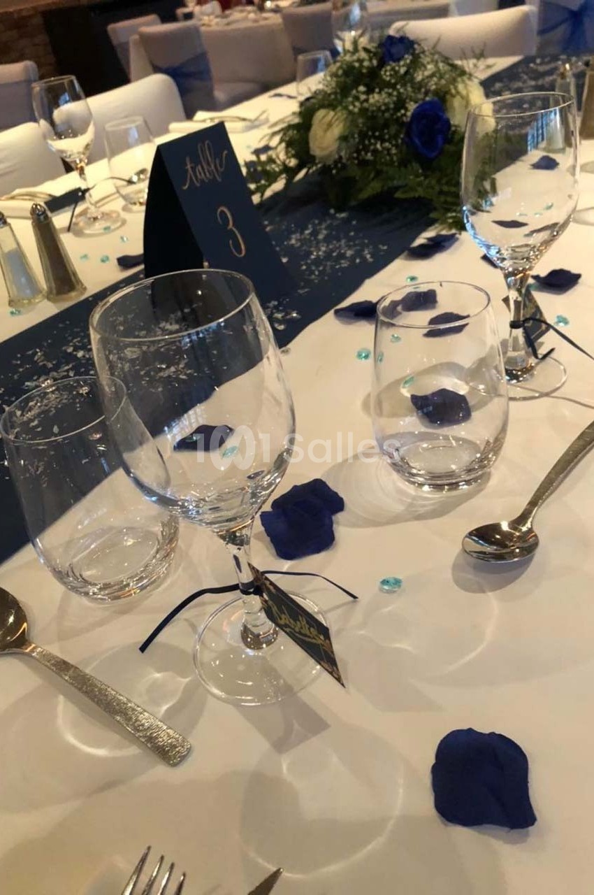 Table de réception élégamment dressée avec nappes blanches, décorations bleues, verres et couverts disposés.