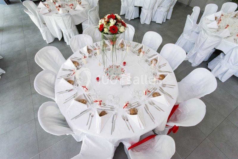 Table ronde décorée pour un événement, avec nappes blanches, couverts disposés et centre de table floral.