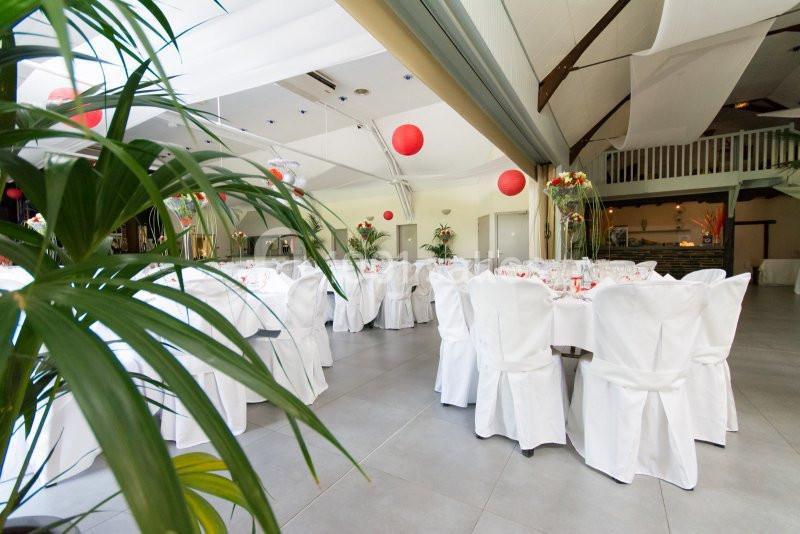 Salle de réception décorée avec des tables rondes, nappes blanches, chaises houssées et lanternes rouges suspendues.
