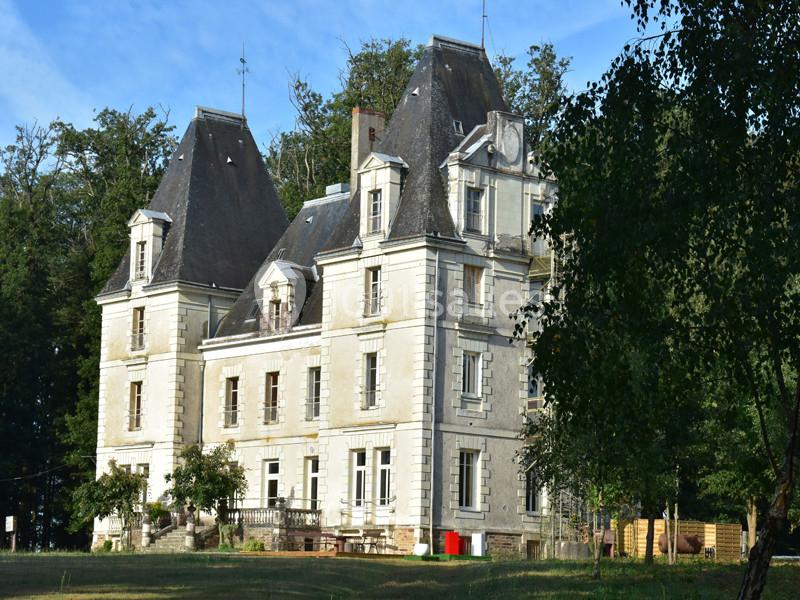 Château en pierre de style classique entouré d'arbres, avec un ciel dégagé en arrière-plan.