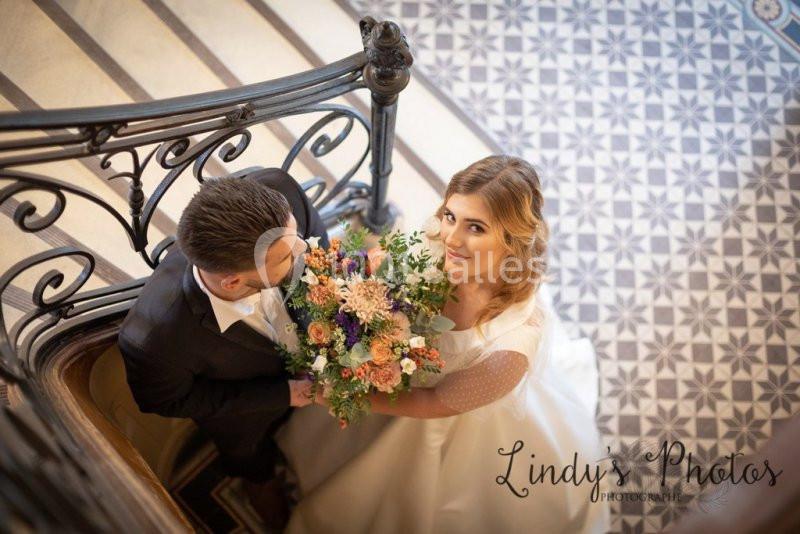Un couple de mariés vu de dessus, tenant un bouquet coloré, sur un escalier en fer forgé et carrelage décoratif.