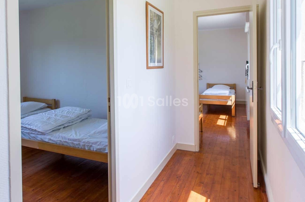 Deux chambres lumineuses avec lits simples, parquet au sol et murs blancs, reliées par un couloir ouvert.