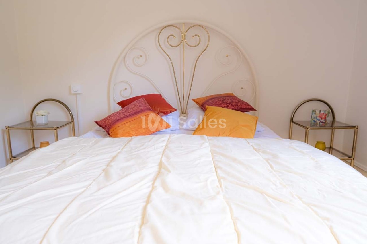 Lit avec une tête de lit en métal décoratif, drap blanc et plusieurs coussins colorés, entouré de tables de chevet.
