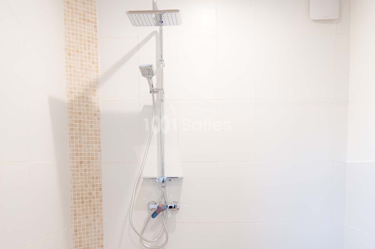 Douche moderne avec colonne équipée d'une pomme haute et d'une douchette, mur carrelé partiellement en mosaïque beige.