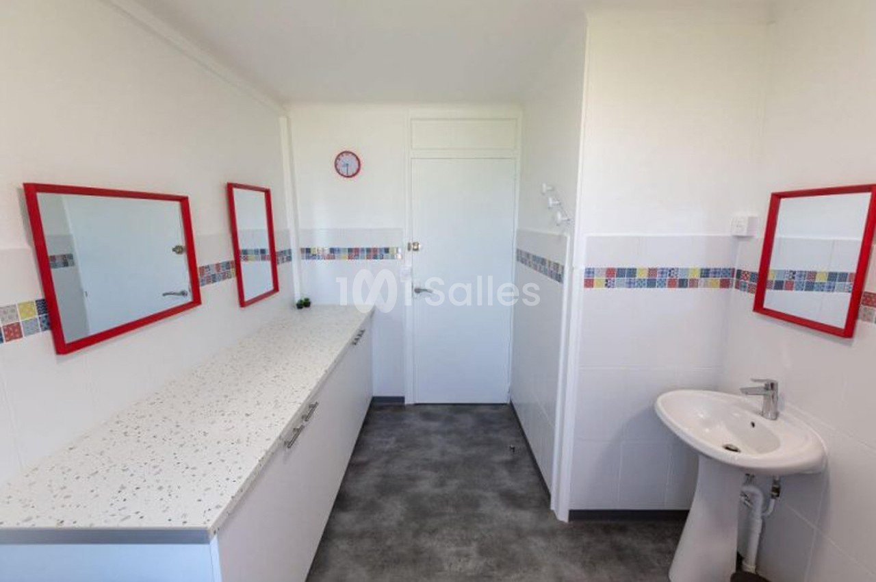 Salle de bain lumineuse avec un sol gris, un lavabo, des miroirs encadrés de rouge et des carreaux colorés en décoration.
