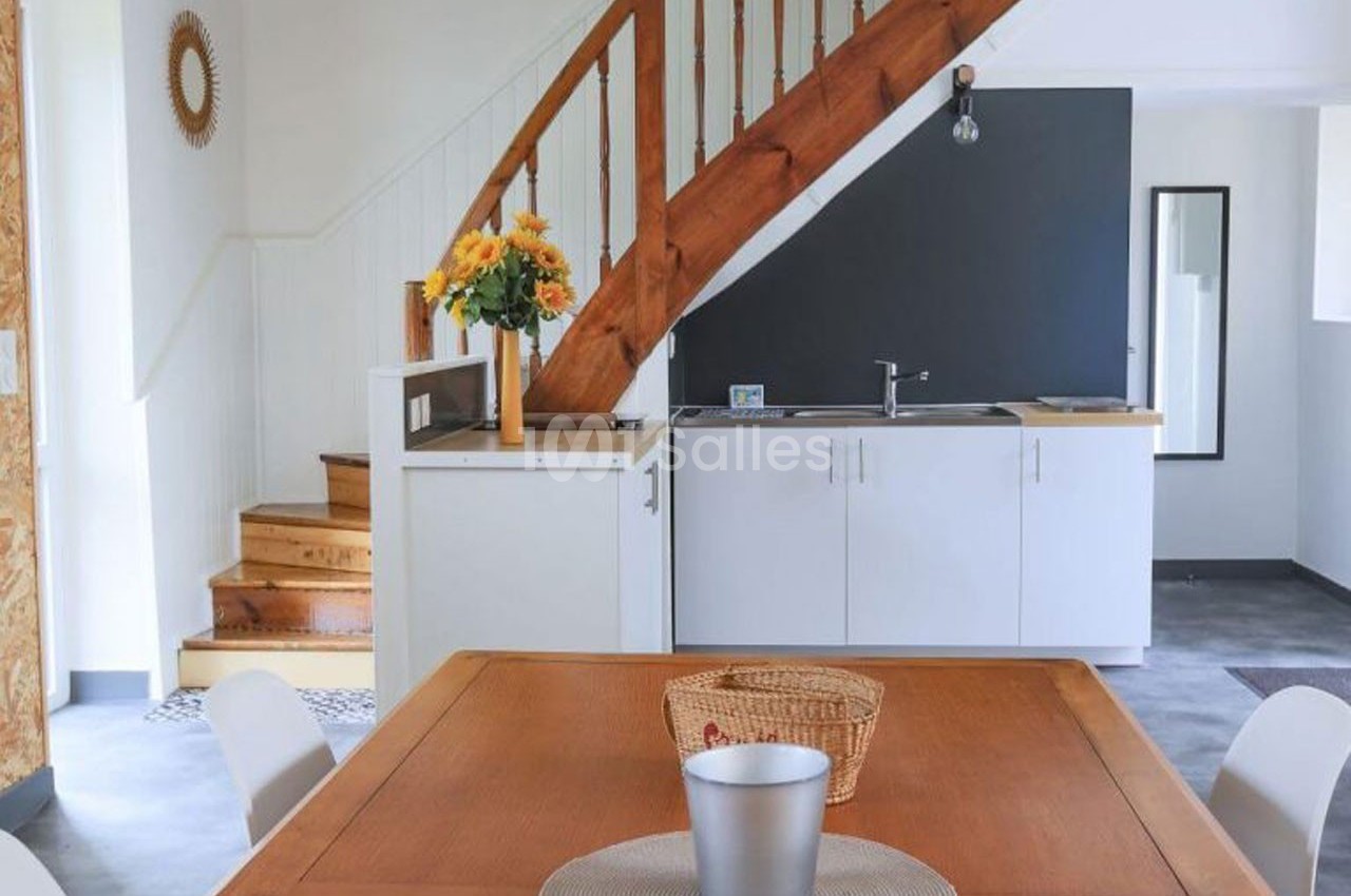 Cuisine ouverte avec escalier en bois, table en bois, bouquet de fleurs jaunes et mur noir en arrière-plan.