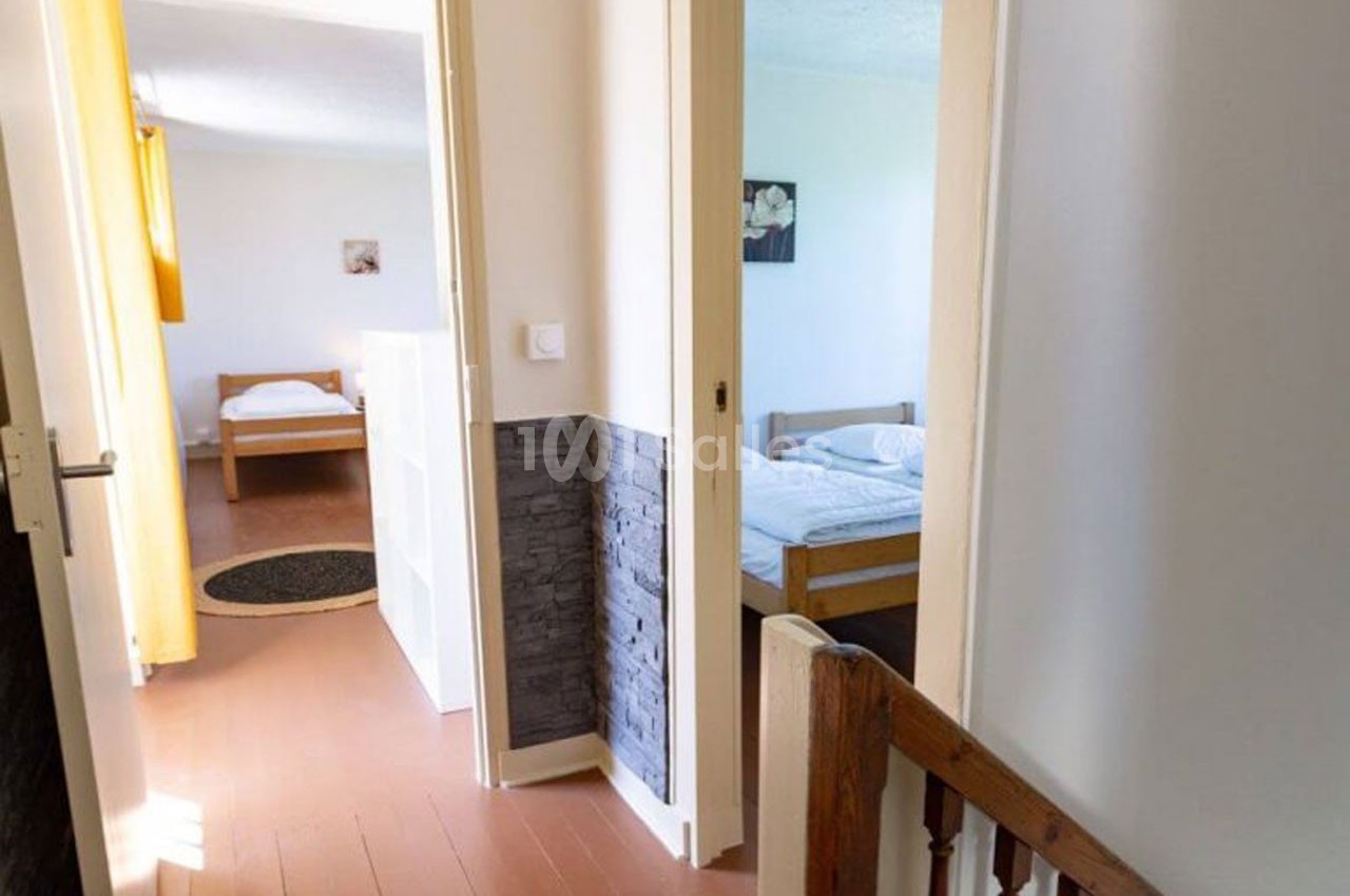 Vue d'un couloir donnant sur deux chambres lumineuses avec lits simples et parquet au sol.