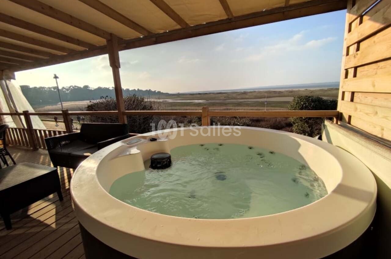 Bain à remous sur une terrasse en bois avec vue sur un paysage naturel de marais et ciel dégagé.