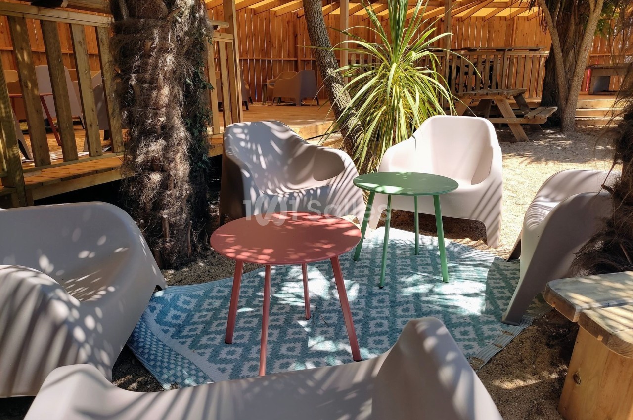 Mobilier de jardin avec fauteuils et tables colorées sur un tapis, entouré de végétation et d'une structure en bois.