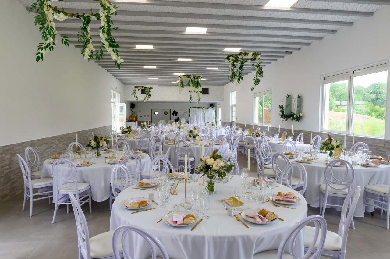 Salle de réception décorée avec des tables rondes dressées, ornées de fleurs et de vaisselle élégante.