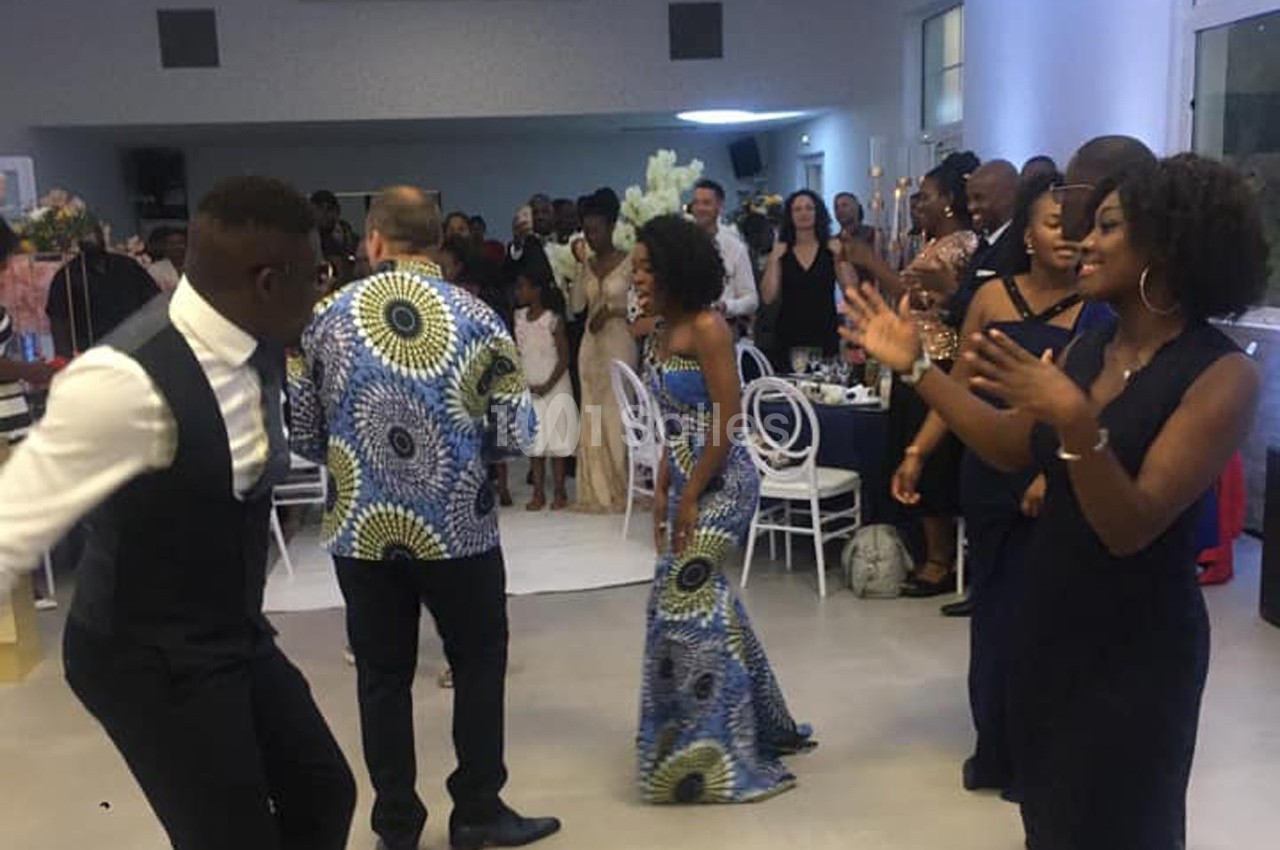 Des personnes dansent et applaudissent lors d'une fête, dans une salle lumineuse avec des invités en arrière-plan.