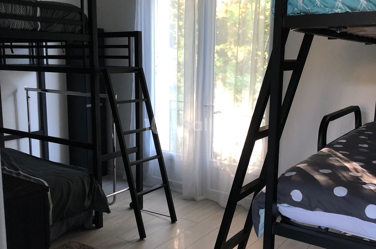 Chambre avec lits superposés, grandes fenêtres laissant entrer la lumière naturelle et parquet clair.