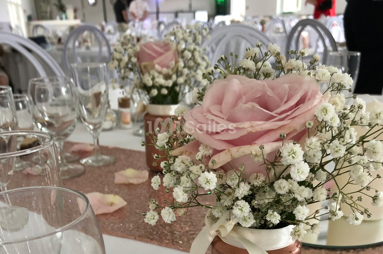 Centre de table avec une rose rose et des gypsophiles dans un vase, entouré de verres et de décorations de mariage.