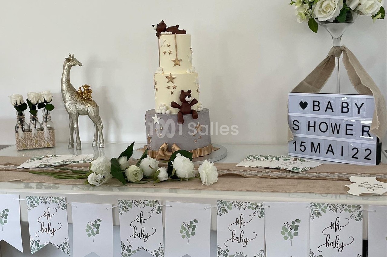 Table décorée pour une baby shower avec gâteau à étages, fleurs blanches, guirlandes et accessoires sur le thème bébé.