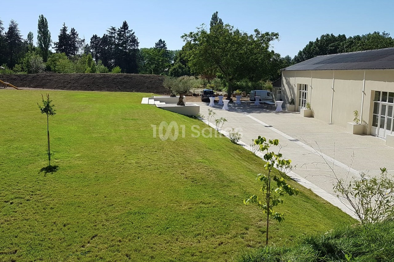 Pelouse bien entretenue bordant une terrasse avec des arbres et un bâtiment clair sous un ciel dégagé.
