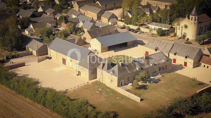 Vue aérienne d'un village avec des bâtiments en pierre, une église et des espaces verts environnants.