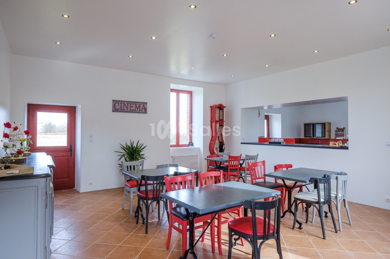 Salle lumineuse avec tables et chaises colorées, décorée d'une enseigne ’cinema’ et d'un comptoir rouge.