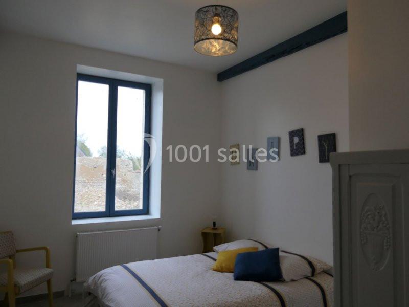 Chambre lumineuse avec lit double, fenêtre donnant sur l'extérieur, mur décoré de cadres et suspension au plafond.