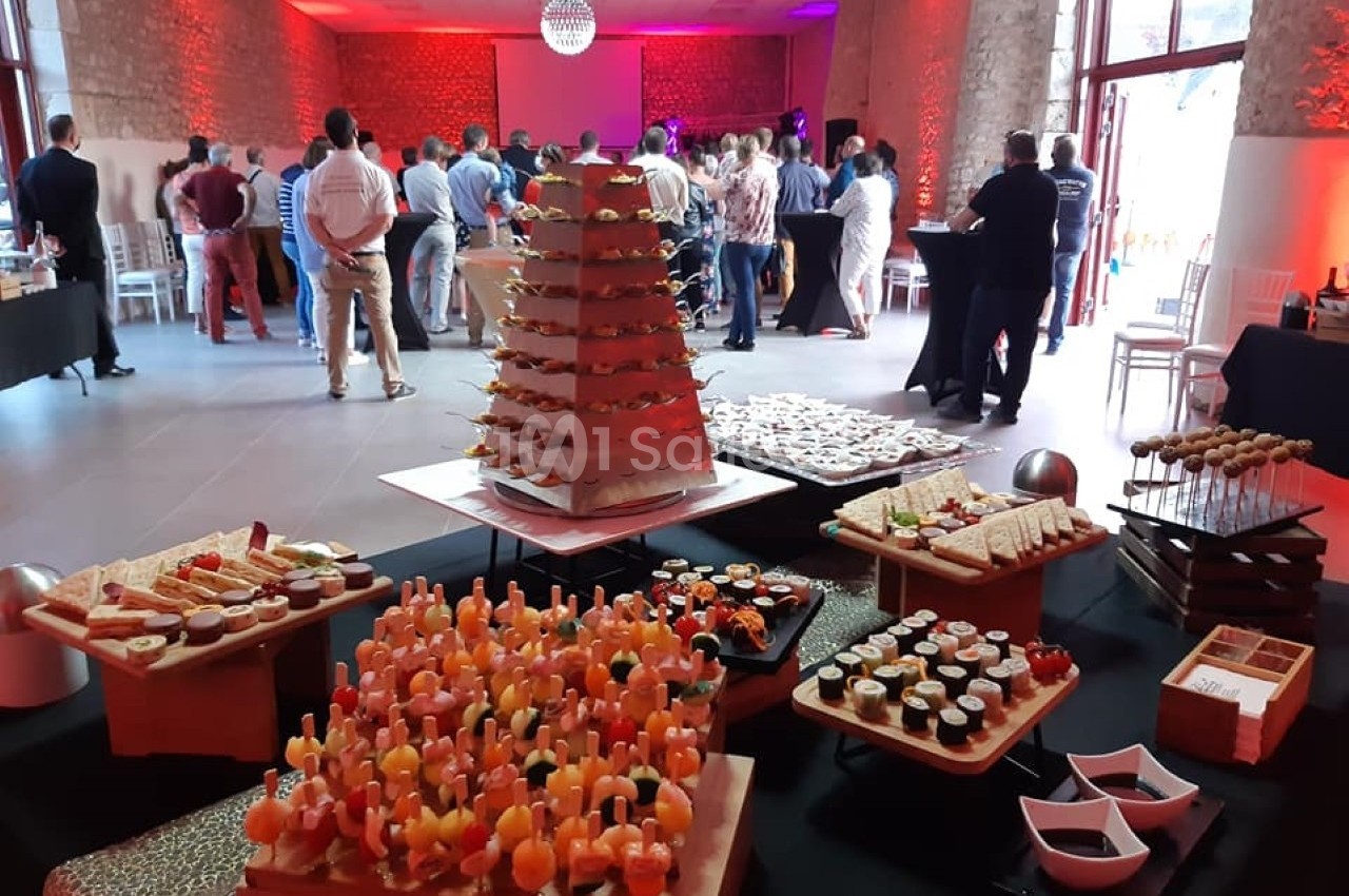 Buffet varié avec amuse-bouches, sushis et brochettes, dans une salle éclairée de lumières rouges, avec des invités debout.