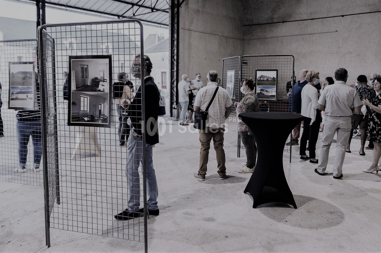 Des personnes visitent une exposition de photographies dans un espace intérieur avec des grilles d'affichage.