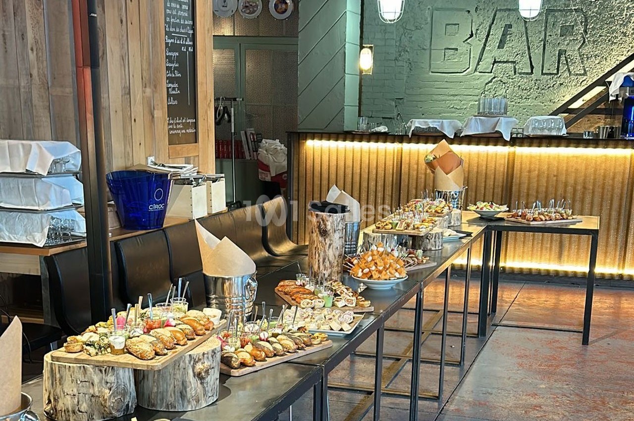 Buffet varié avec des plats disposés sur des tables dans un espace de bar au décor industriel.