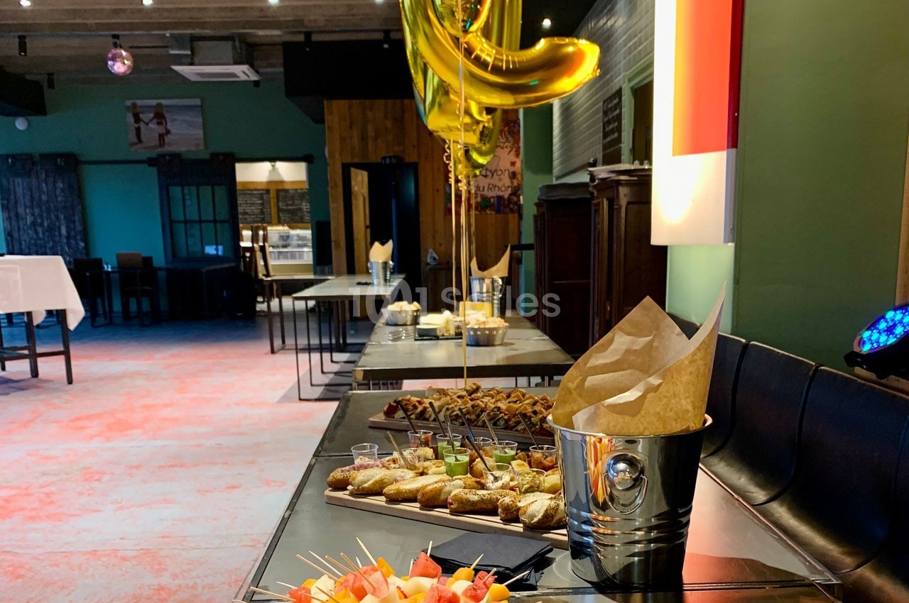 Buffet avec amuse-bouches variés, brochettes de fruits et décorations, dans une salle de réception lumineuse.