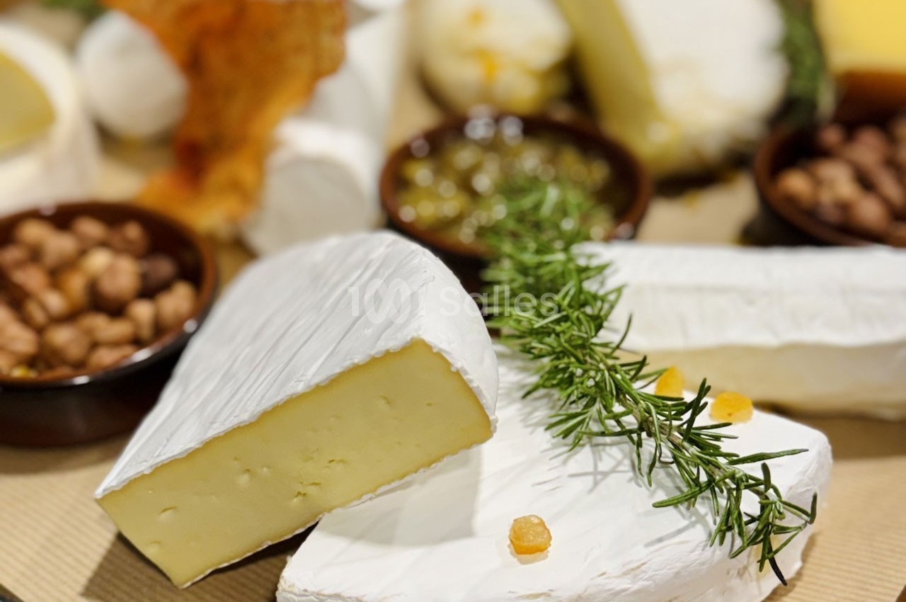 Assortiment de fromages à pâte molle avec garnitures, herbes fraîches et accompagnements en arrière-plan.