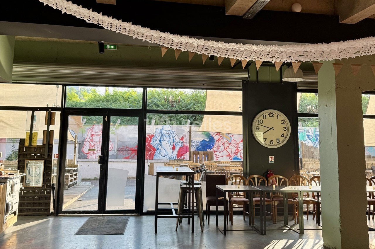 Intérieur d'un café lumineux avec des tables en bois, une grande horloge murale et une vue sur une terrasse décorée de…