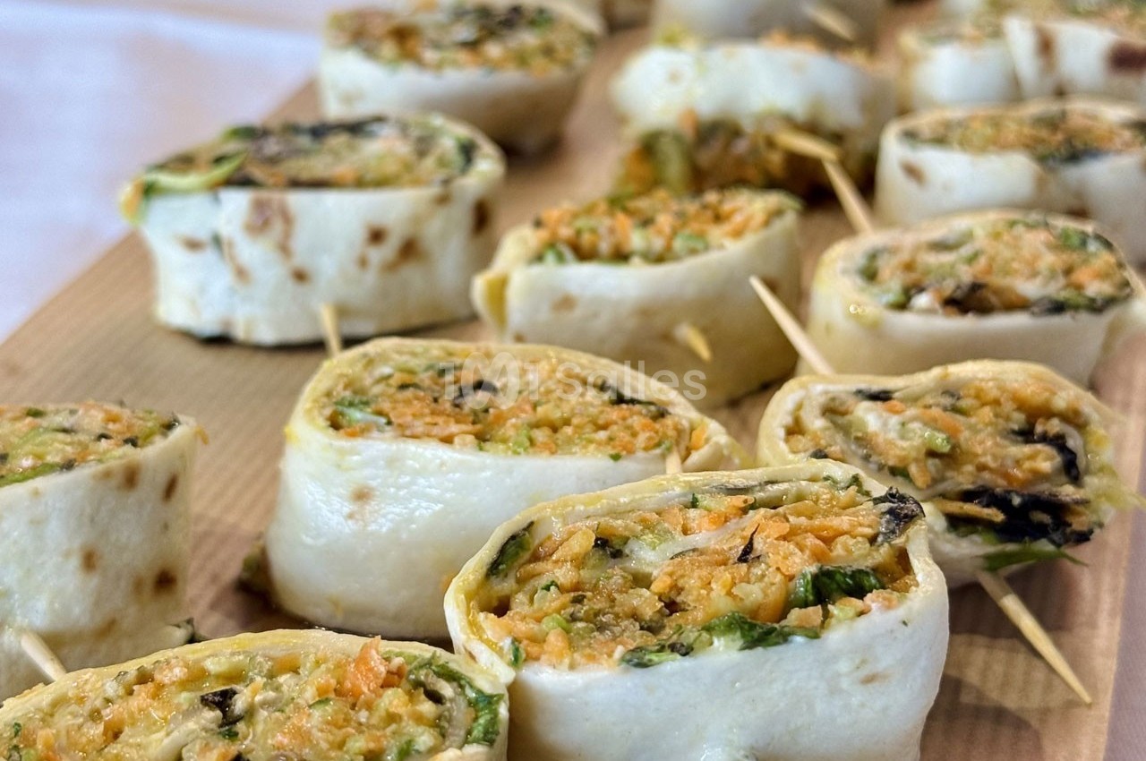 Roulés de tortillas garnis de légumes râpés et herbes, présentés en bouchées sur une planche en bois.