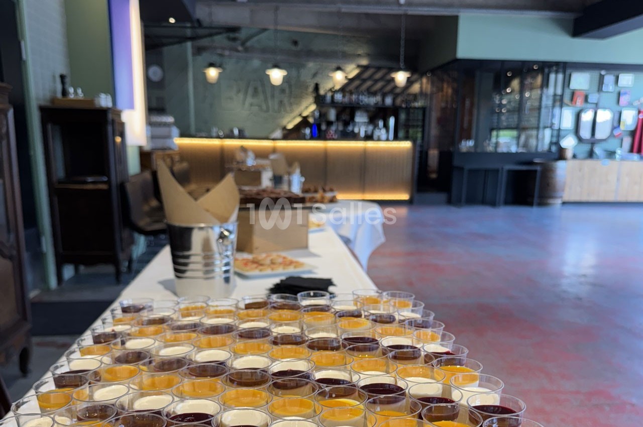 Buffet avec des verrines colorées en premier plan, dans une salle avec un bar en arrière-plan.