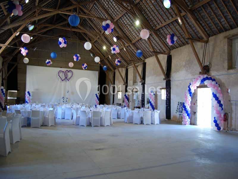 Salle de réception décorée avec des ballons colorés, des tables rondes dressées et un écran blanc en fond.