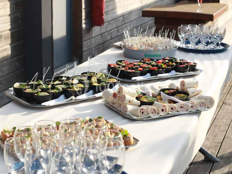Buffet avec plateaux de verrines, wraps et amuse-bouches, disposés sur une table blanche en extérieur.