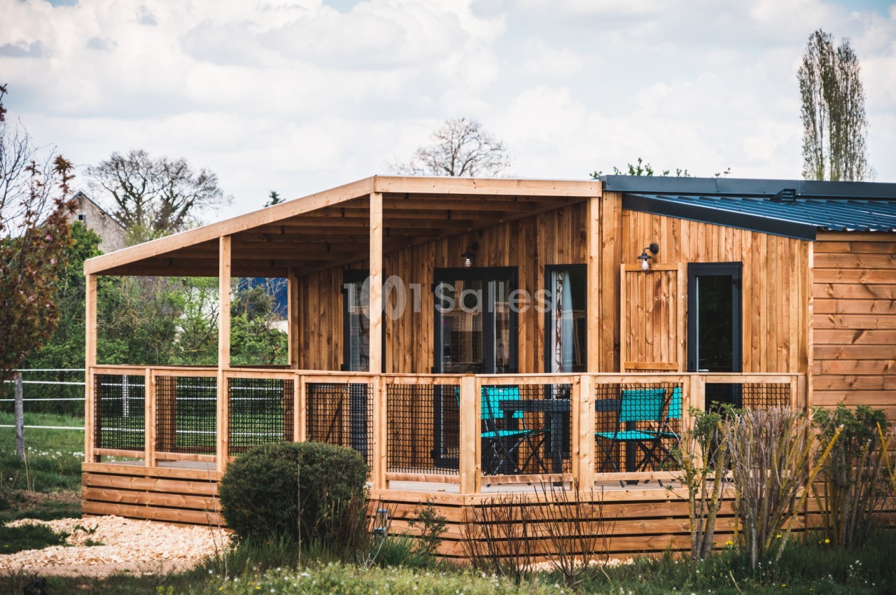 Chalet en bois avec terrasse couverte, entouré de végétation et situé dans un environnement rural.