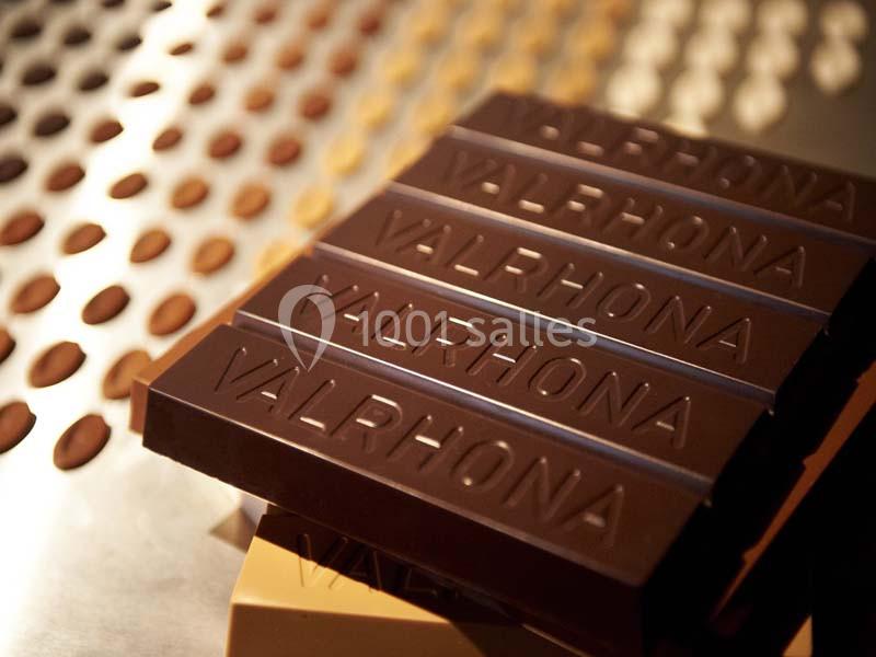 Tablettes de chocolat noir marquées ’Valrhona’ posées sur une surface métallique perforée.