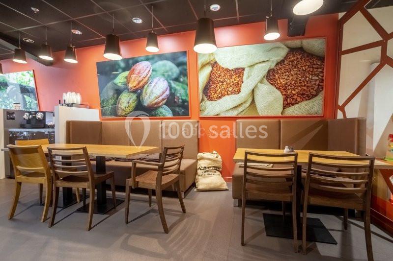 Salle de restaurant avec tables en bois, banquettes, et décorations murales représentant des fèves de cacao.