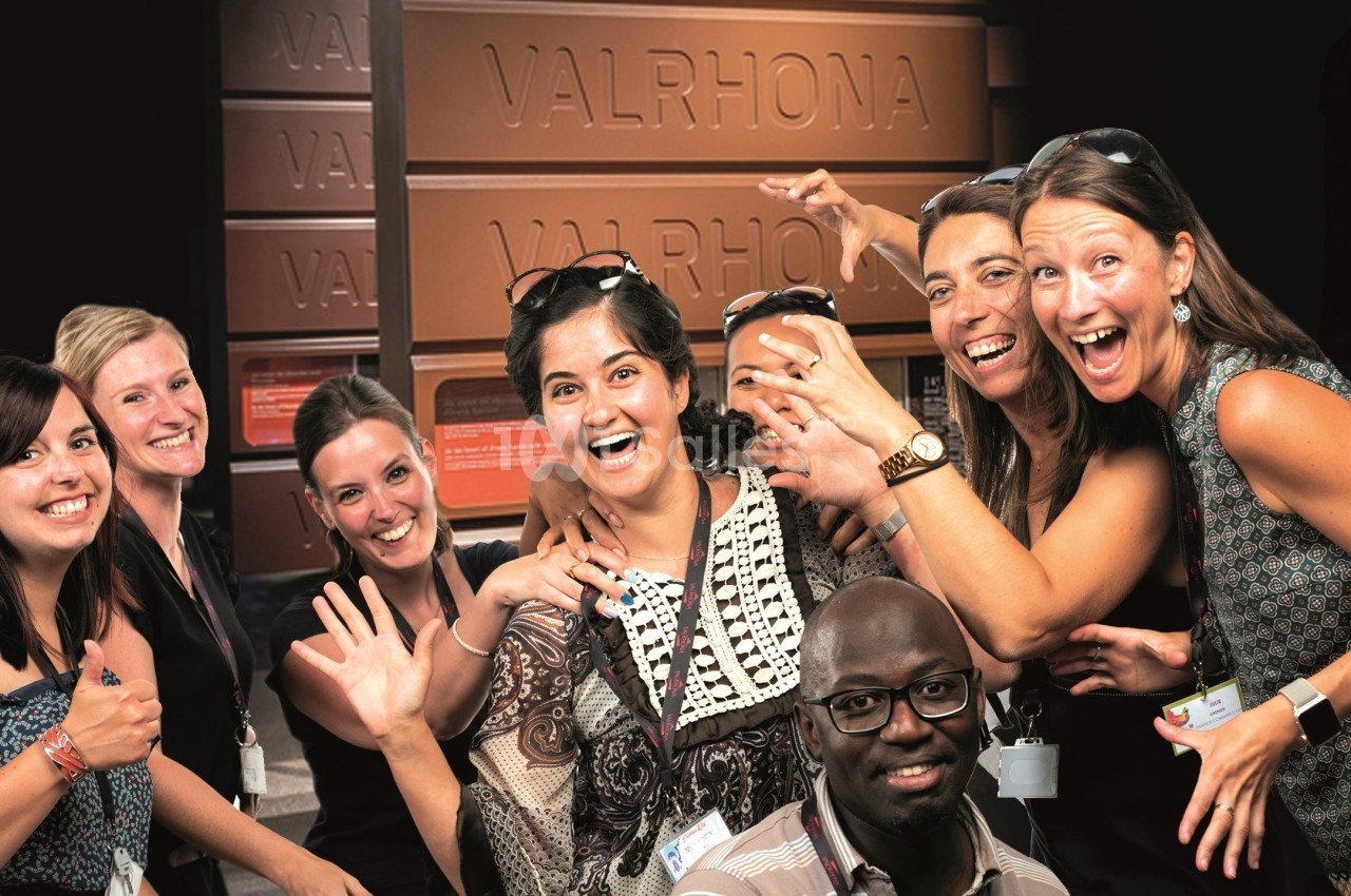 Un groupe de personnes souriantes posant devant une grande sculpture en forme de tablette de chocolat Valrhona.
