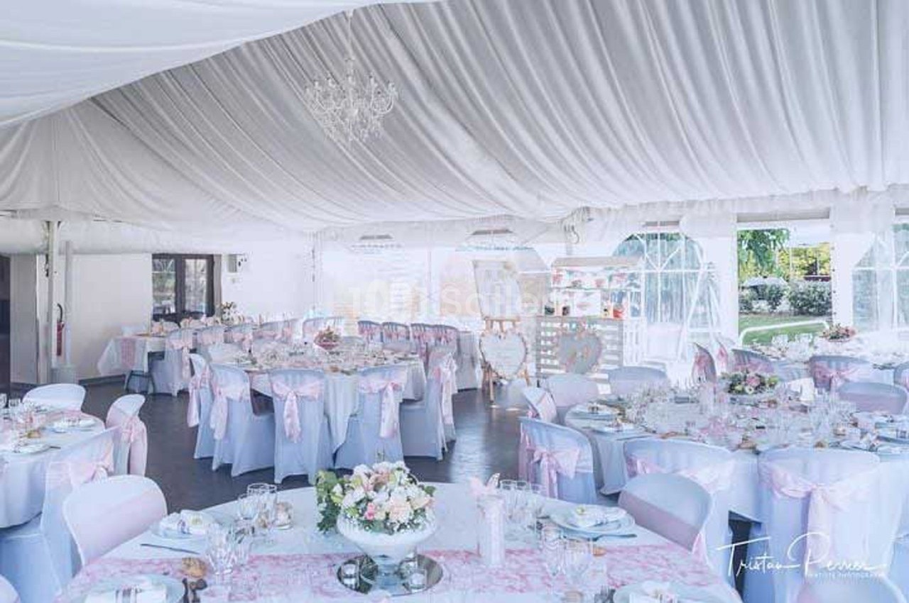 Salle de réception décorée dans des tons pastel avec des tables dressées et des chaises ornées de nœuds roses.