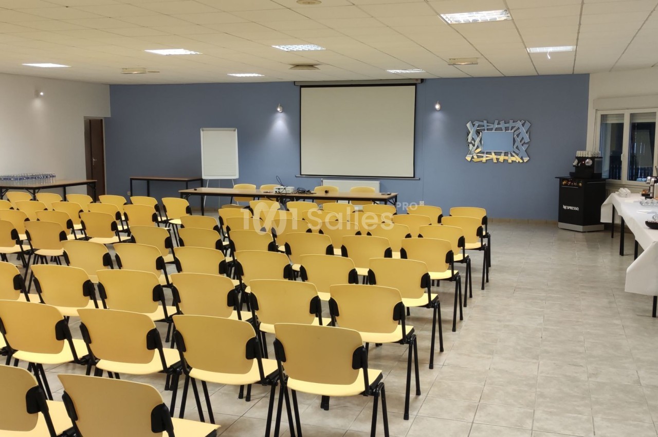 Salle de conférence avec des rangées de chaises jaunes, un écran de projection et une table de collation sur le côté.
