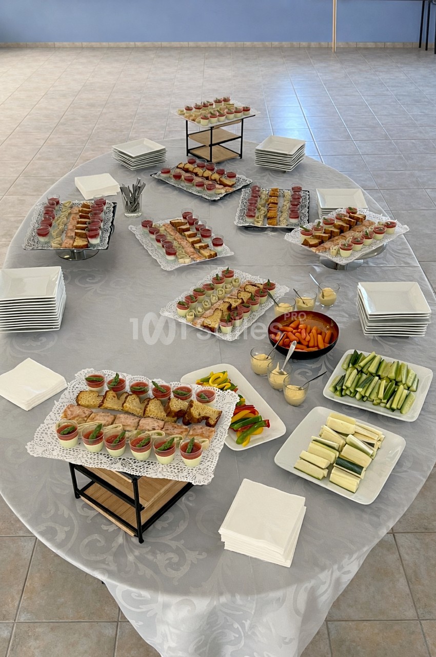 Table dressée avec des amuse-bouches variés, légumes frais, sauces et piles d'assiettes sur une nappe blanche.