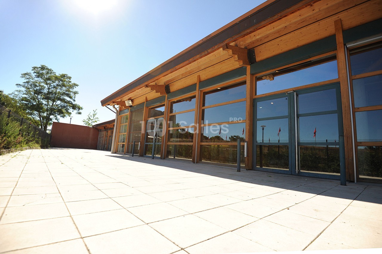 Bâtiment moderne avec façade en bois et grandes baies vitrées donnant sur une terrasse ensoleillée.