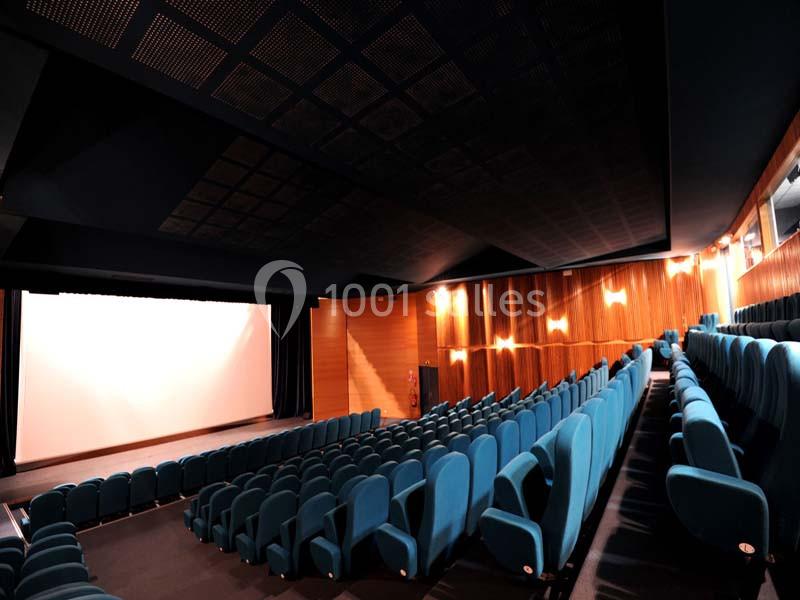 Salle de cinéma vide avec des rangées de sièges bleus et un écran blanc illuminé à l'avant.